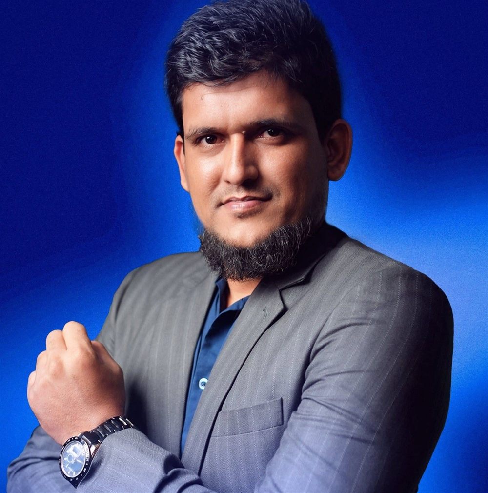 Kausar Rony in a grey pinstripe suit against a blue studio backdrop